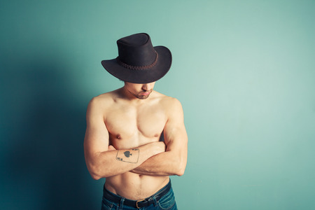A sexy shirtless cowboy is posing by a blue wallの写真素材