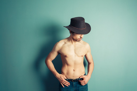 A sexy shirtless cowboy is posing by a blue wallの写真素材