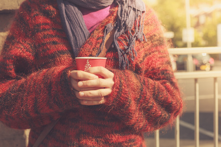 A young woman is standing in the street with a paper cup in her hand on a sunny dayの写真素材