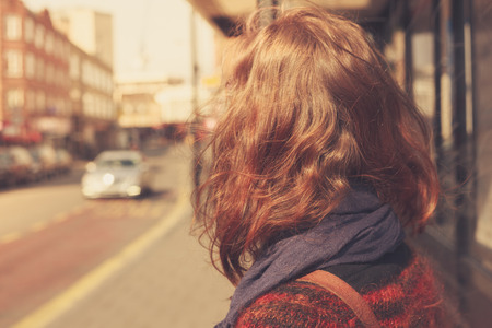 A young woman is waiting at the bus stop on a sunny dayの写真素材