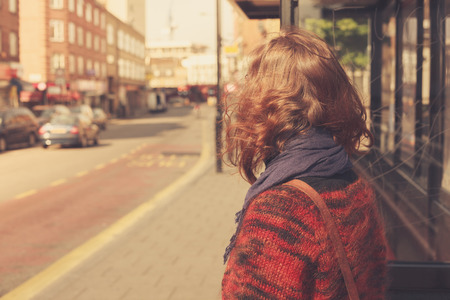 A young woman is waiting at the bus stop on a sunny dayの写真素材