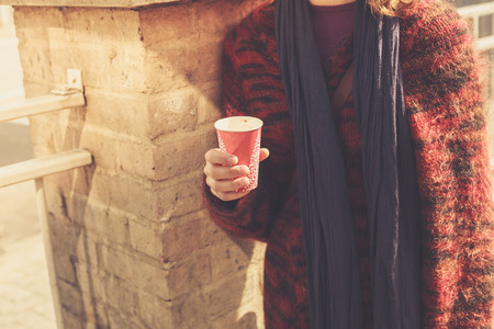 A young woman is standing in the street on a sunny day and holding a paper cupの写真素材