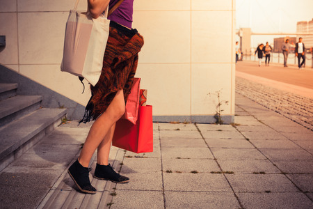 A young woman with shopping bags is standing by some stairs outside at sunsetの写真素材