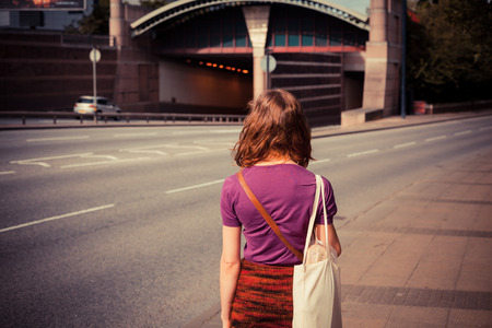 A young woman is walking by the side of a busy road on a sunny afternoonの写真素材