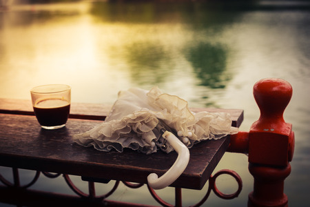 A glass of coffee and an umbrella on a wooden table by a lake in the afternoonの写真素材