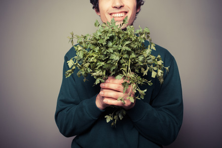A happy young man is holding a big bunch of fresh parsleyの写真素材