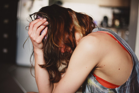 A sad young woman is sitting in her kitchen with a headacheの写真素材