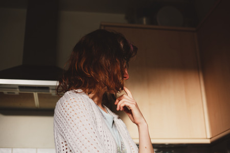 A young woman is standing at home in her kitchen and thinkingの写真素材