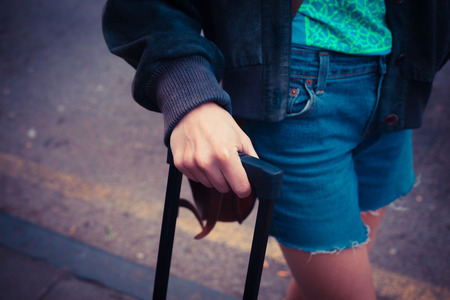 A young woman is standing in the street with a suitcaseの写真素材