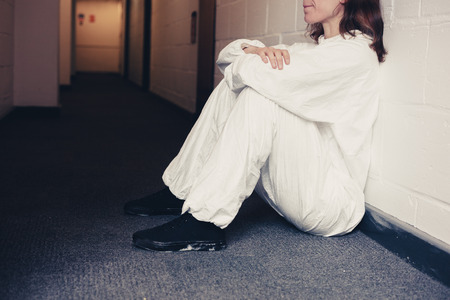 Young woman wearing a boiler suit is upset and is sitting in a corridorの写真素材