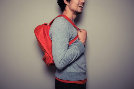 A happy young student is wearing a red backpack and is smiling