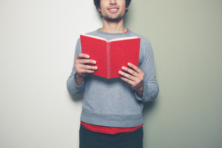 A young man is standing against a split colored green and white background and holding a red bookの写真素材