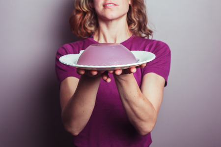 A young woman in a purple top is presenting a plate of jellyの写真素材