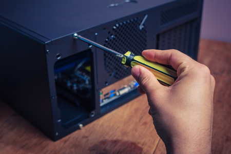 A hand is opening a computer case with a screwdriverの写真素材