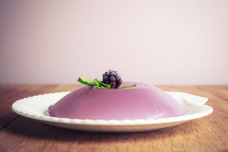 Closeup on a purple jelly pudding with a blackberry and mint leaves on topの写真素材