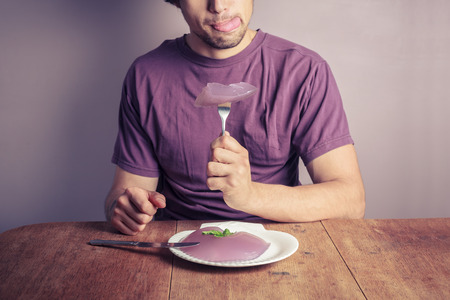 A young man is sitting at a table and eating a purple jelly puddingの写真素材