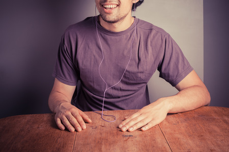 A young man is sitting at a table with earphones in his ears and is listening to musicの写真素材
