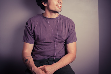 A happy young man is listening to music through his earphonesの写真素材