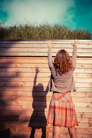 A young woman is standing in a garden outside a woden cabin and is looking upの写真素材