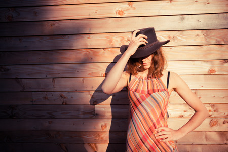 A young woman wearing a cowboy hat is standing outside a wooden cabinの写真素材
