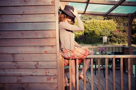 A young woman wearing a cowboy hat is sitting on the porch of a cabinの写真素材