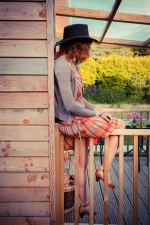A young woman wearing a cowboy hat is sitting on the porch of a cabinの写真素材