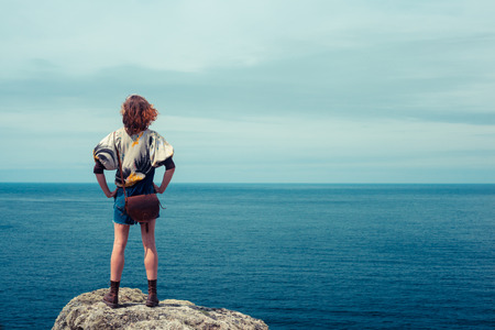A young woman is standing on a rock by the seaの写真素材