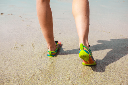 Closeup on the feet of a young woman wearing trainers as she is walking on the beachの写真素材