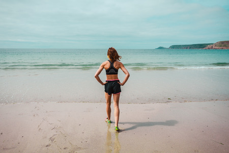 A fit young woman is standing on the beach and looking at the seaの写真素材