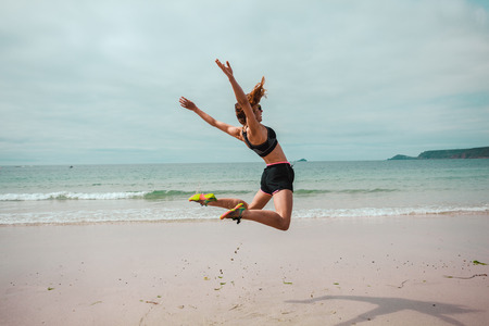 A young woman is doing star jumps on the beach by the seaの写真素材