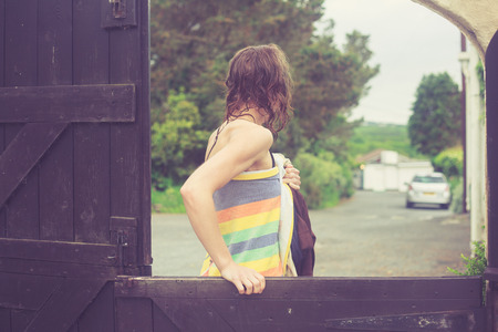 A young woman wrapped in a towel is closing a gate outside on a farmの写真素材
