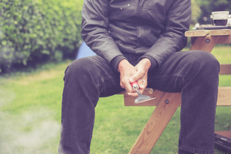 A senior man is looking after a barbecue outside in a gardenの写真素材