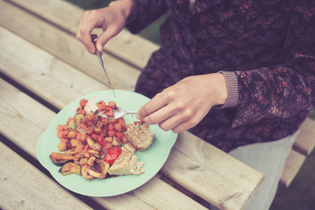 A young woman is eating at a barbecue outside in the eveningの写真素材
