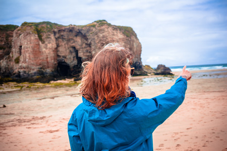 A young woman is walking on the beach and pointing at the oceanの写真素材