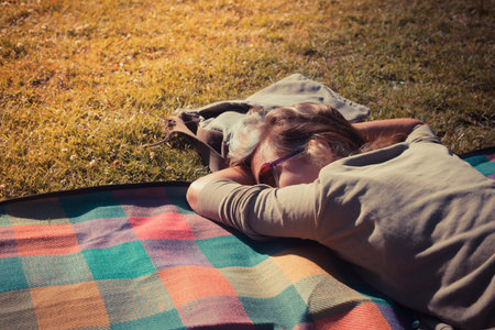 A young woman is relaxing on a blanket at sunset in a parkの写真素材
