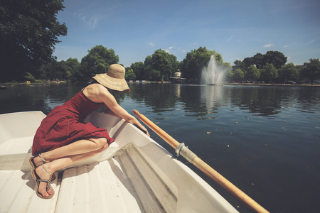A young woman is sitting in a boat on the lake and is relaxing on a sunny dayの写真素材