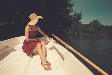 A young woman is sitting in a rowing boat and is looking at the lakeの写真素材