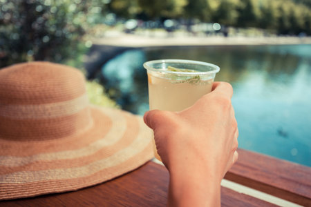 A young woman is drinking lemonade by a pond in the parkの写真素材