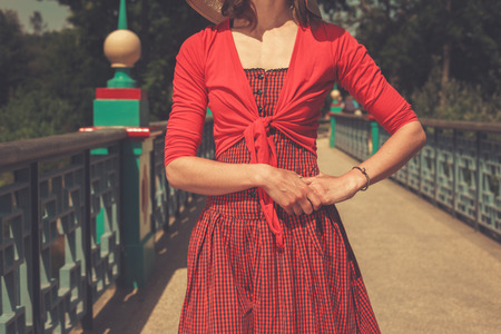 A young woman wearing a red dress is standing on a bridge in a parkの写真素材