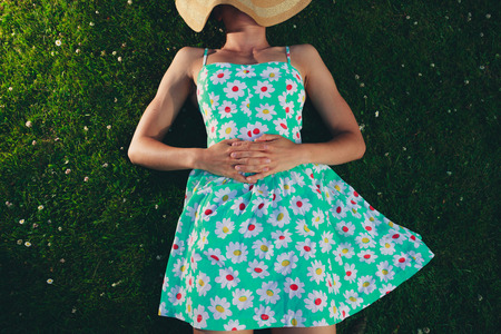 A young woman wearing a dress and a hat is lying on the grass in the parkの写真素材
