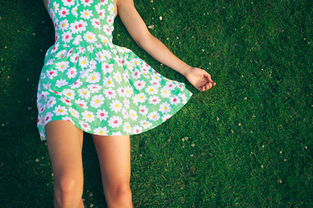 A young woman wearing a flowery dress is lying on the grass in summerの写真素材
