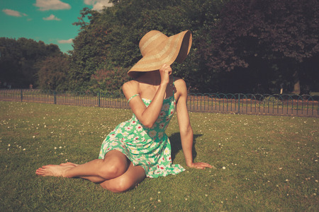 A young woman wearing a dress and a hat is sitting on the grass in a parkの写真素材