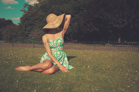 A young woman wearing a dress and a hat is sitting on the grass in a parkの写真素材
