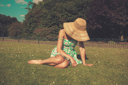 A young woman wearing a dress and a hat is sitting on the grass in a parkの写真素材