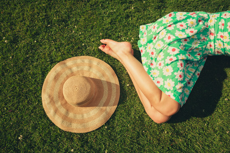 A young woman wearing a dress is sleeping on the grass with a hat next to herの写真素材