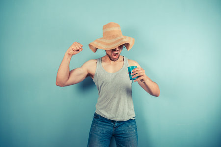 A happy young man wearing a beach hat is drinking from a blue cup