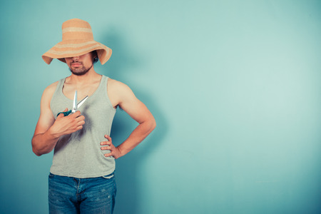 A young man wearing a large beach hat is holding a pair of scissorsの写真素材