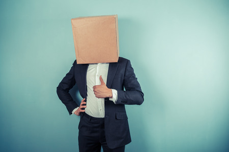 A businessman with a box on his head is giving thumbs upの写真素材