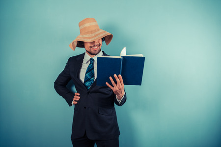 A businessman wearing a beach hat is reading a bookの写真素材