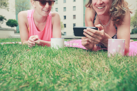 Two young women are laughing and smiling as they look at a phone outsideの写真素材